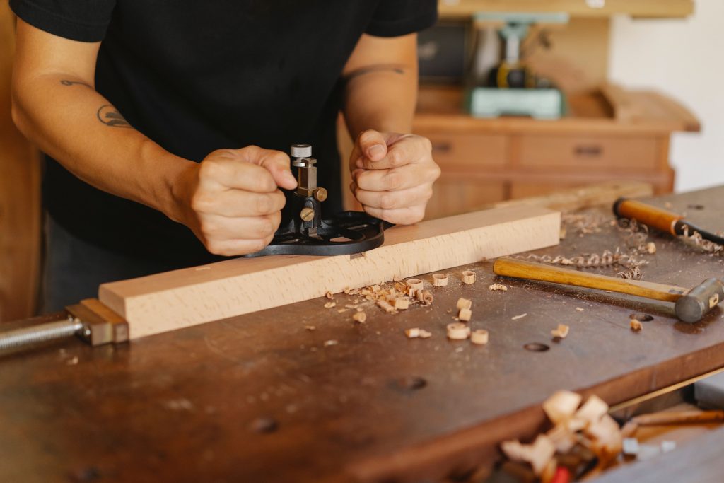 Crop anonymous craftsman working at workbench with manual router plane for making holes in wooden plank in joinery